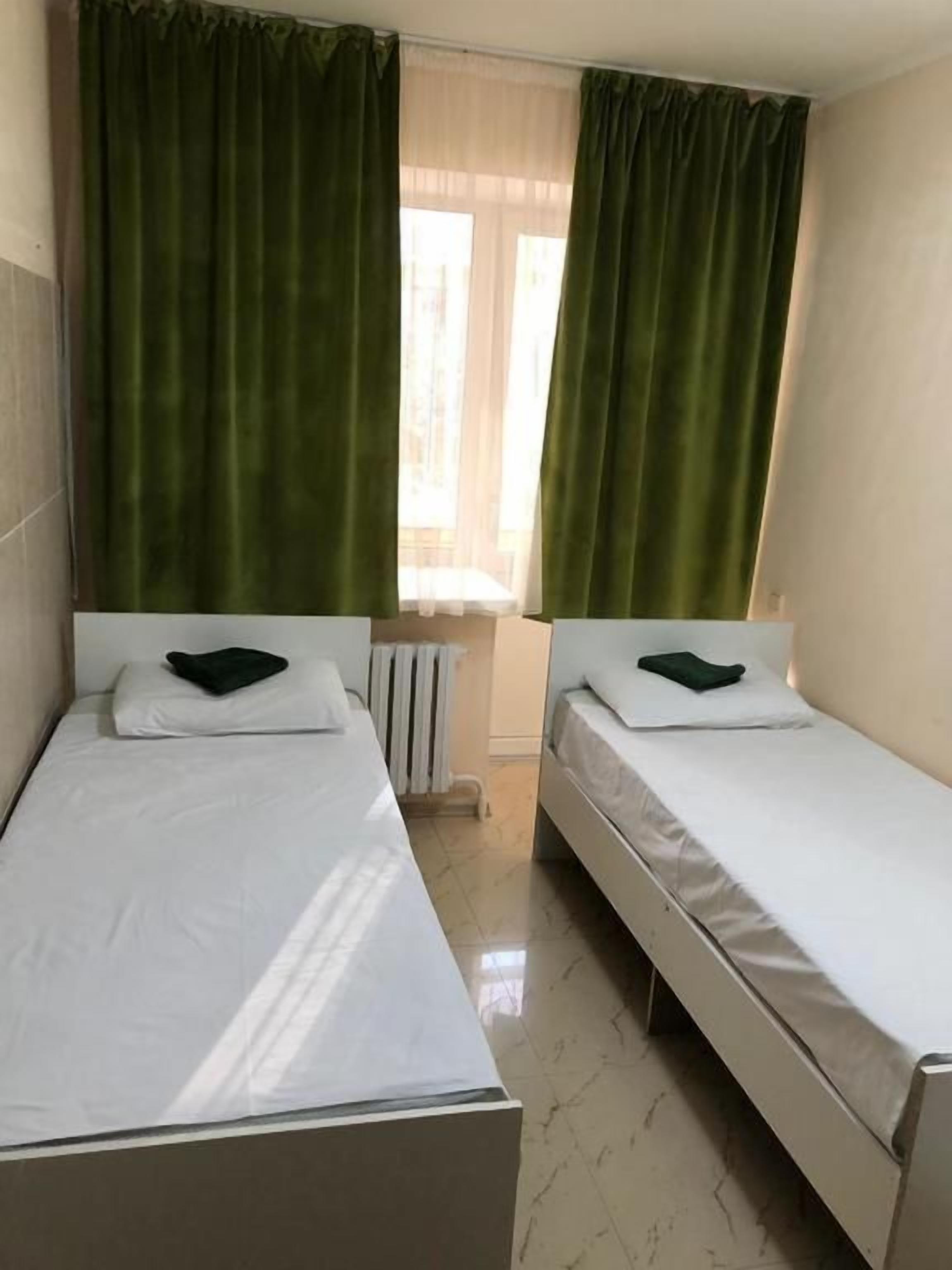 A room with two single beds, a radiator, and a window with curtains.
