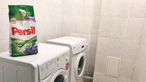 A front-loading washing machine and dryer in a laundry room with a bag of Persil detergent on the dryer. - Elite Hostel (Astana)