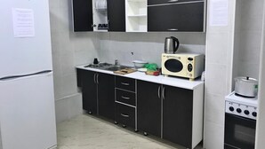 A compact kitchen with a white refrigerator, black cabinets, a microwave, and a small oven. - Elite Hostel (Astana)