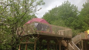 A wooden deck with a red roof, surrounded by trees and greenery. - Apple Dome at Cabot Shores Wilderness Resort (Englishtown)
