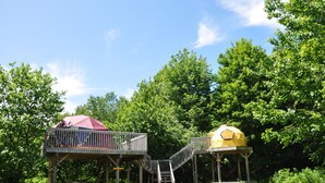 A wooden deck with a red umbrella and a yellow dome structure. - Apple Dome at Cabot Shores Wilderness Resort (Englishtown)