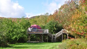 A treehouse with a covered upper deck and a staircase. - Apple Dome at Cabot Shores Wilderness Resort (Englishtown)