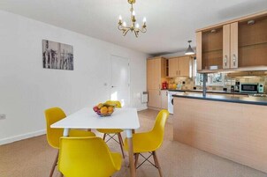 Cocina moderna con armarios de madera, encimera blanca y zona de comedor con mesa blanca y sillas amarillas.