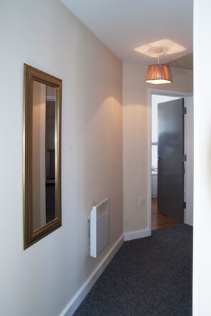 Un couloir avec un radiateur, un miroir et une porte donnant sur une salle de bain.