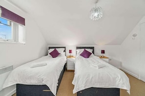 A bedroom with two single beds, each with a pillow and a bedside table with a lamp.