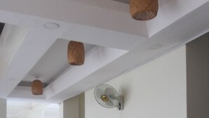 Quarto espaçoso com teto alto, ventoinha no teto e luminária fixada na parede. Há uma cadeira preta e uma cadeira azul no quarto.
