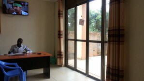 Quarto com uma janela grande, escrivaninha, cadeira e televisão na parede.
