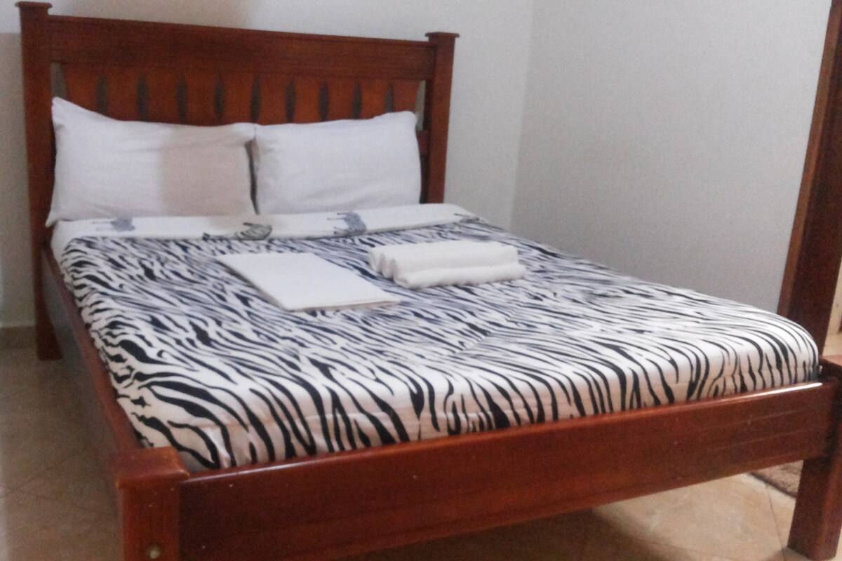 A bed with a zebra print bedspread, two pillows, and a folded towel.