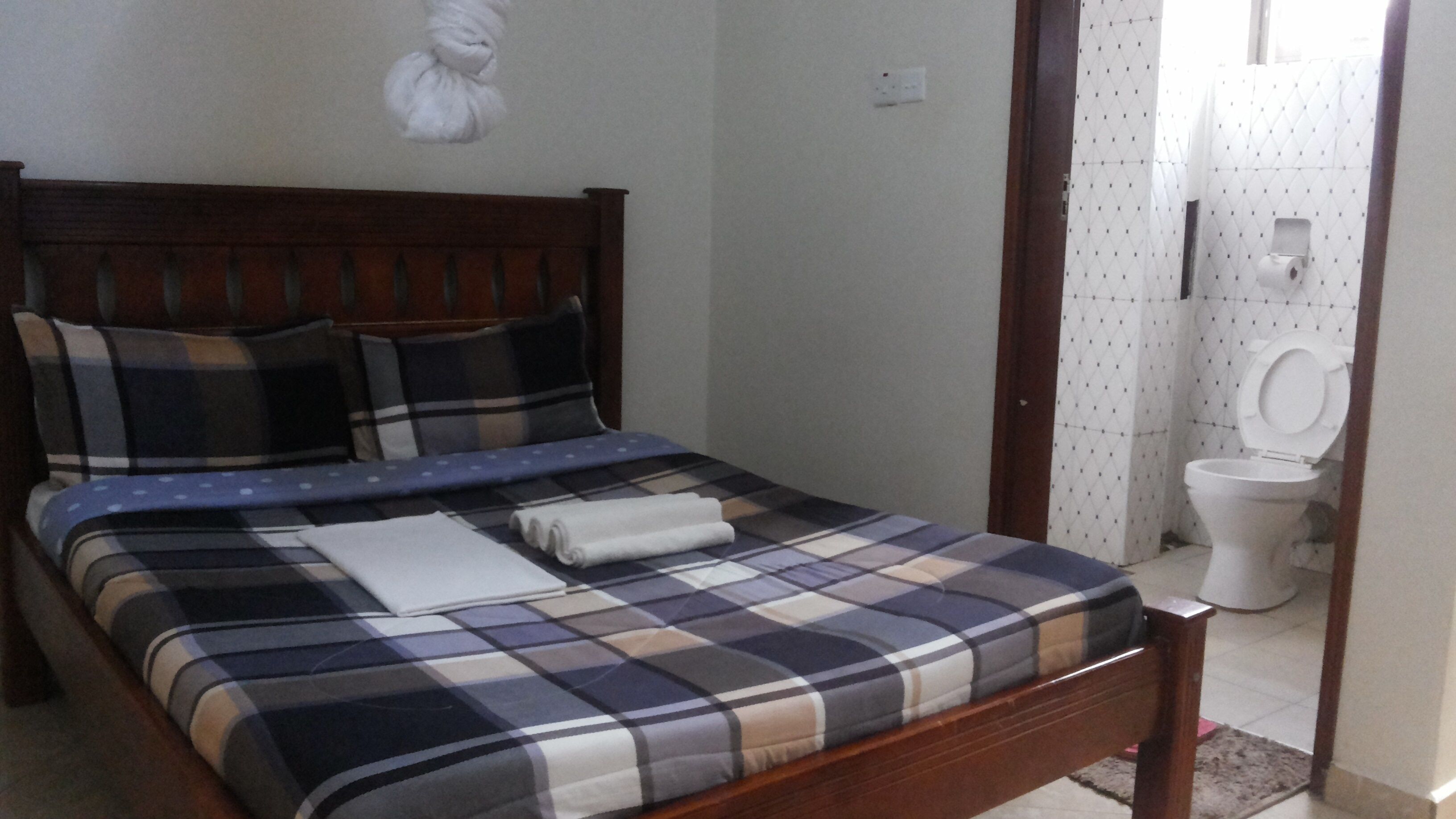 A bedroom with a wooden bed, a blue and white checkered bedspread, and a white towel on the bed.