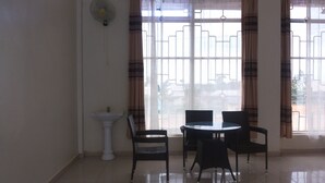 Quarto com pia branca, duas cadeiras, uma mesa redonda e uma janela com cortinas.