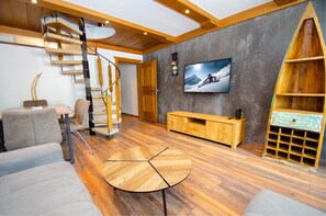 A modern living room with a spiral staircase, a flat-screen TV, wooden furniture, and a large window. - Penthouse 81 Kaprun (Kaprun)