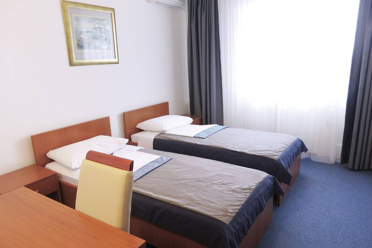A hotel room with two single beds, a wooden desk, a chair, and a framed picture on the wall.
