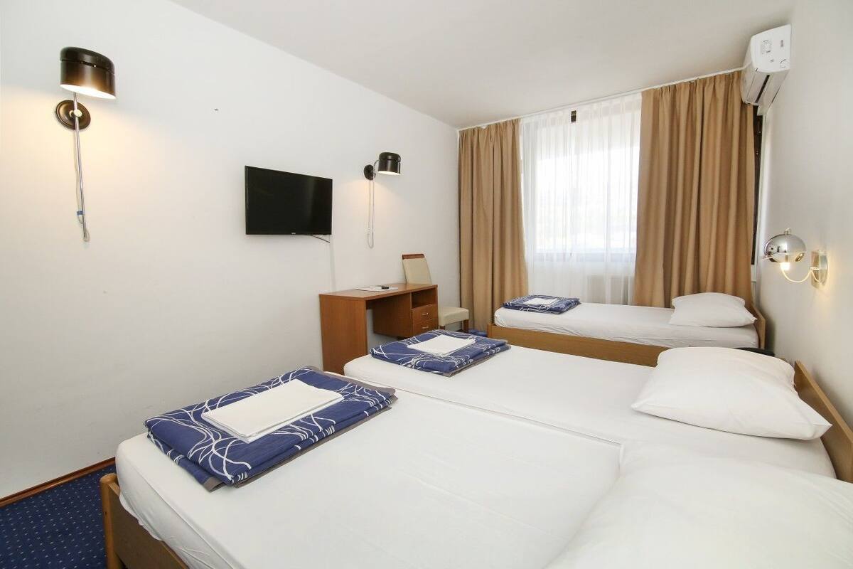A hotel room with two beds, a desk, a TV, and an air conditioning unit.