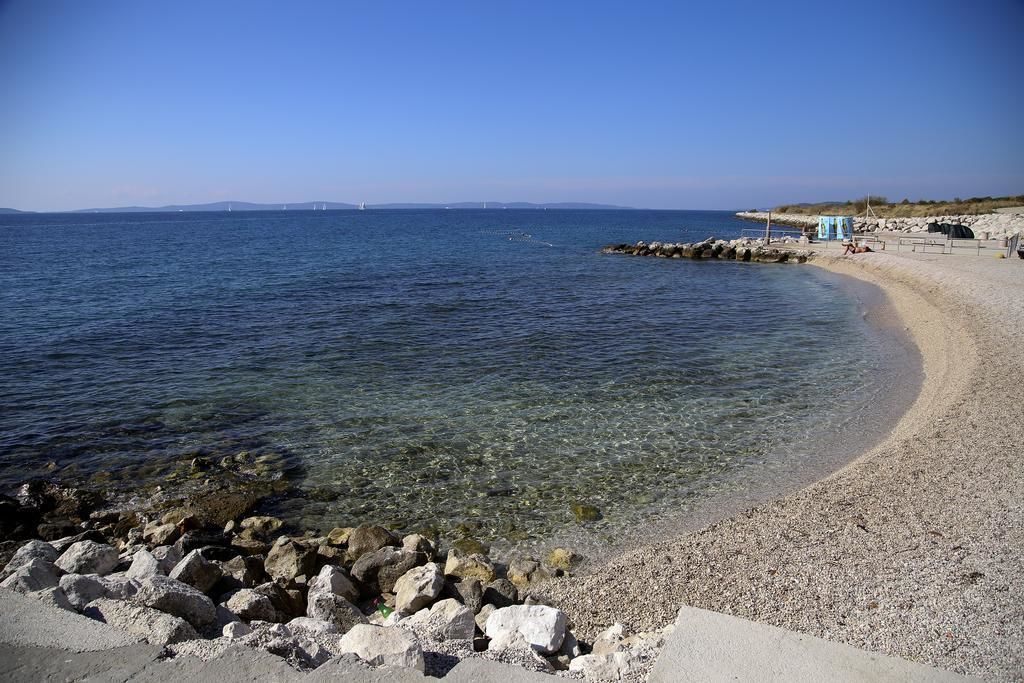 A beach with clear water, a rocky shoreline, and a small structure on the right.