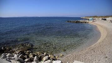 A beach with clear water, a rocky shoreline, and a small structure on the right.
