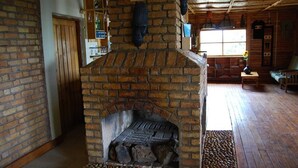A rustic interior with a brick fireplace, wooden shelves, and a cozy seating area. - Rihuja Safari Lodge (Bwindi)