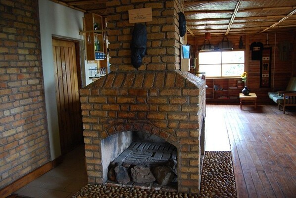 A rustic interior with a brick fireplace, wooden shelves, and a cozy seating area.