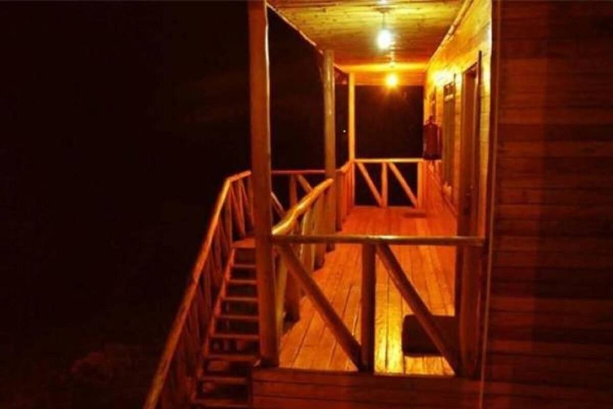 Uma escadaria de madeira leva a uma varanda com guarda-corpo, um deck de madeira e um acessório de iluminação sobre o deck.