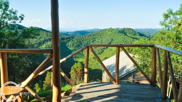 A wooden deck with a view of a lush green valley and distant hills. - Rihuja Safari Lodge (Bwindi)
