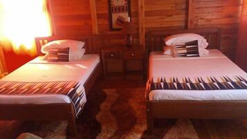 Una habitación con dos camas individuales, paredes de madera, una mesita y una lámpara.