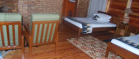 A room with a brick wall, a bed with a patterned bedspread, a wooden chair, and a small table.
