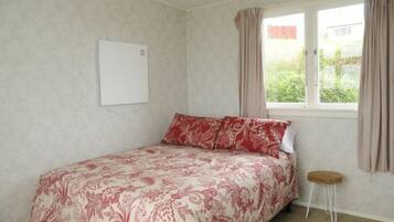 A bedroom with a bed, a small stool, a window with curtains, and a whiteboard on the wall.