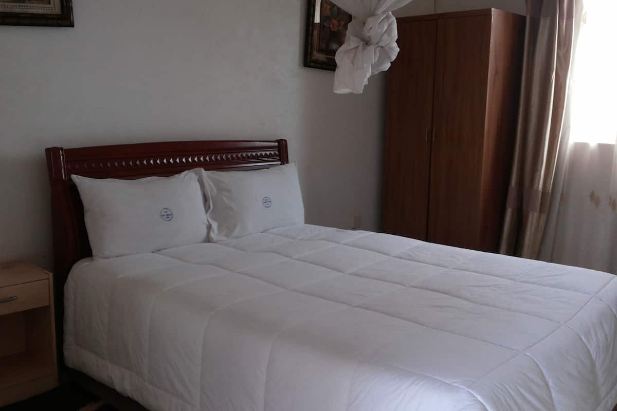 Una cama bien hecha con cabecera y mesita de noche de madera, además de un armario de madera.
