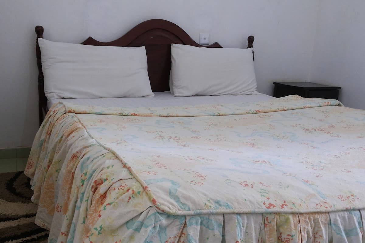 Una cama con colcha estampada, dos almohadas blancas, cabecera de madera y una mesita de noche.