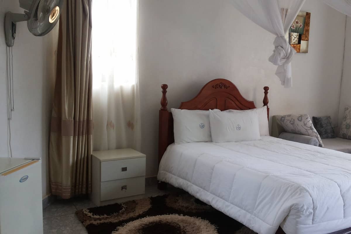 Un dormitorio con cama de madera, ropa de cama blanca, una mesita de noche y un espejo decorativo, además de un ventanal con cortinas.