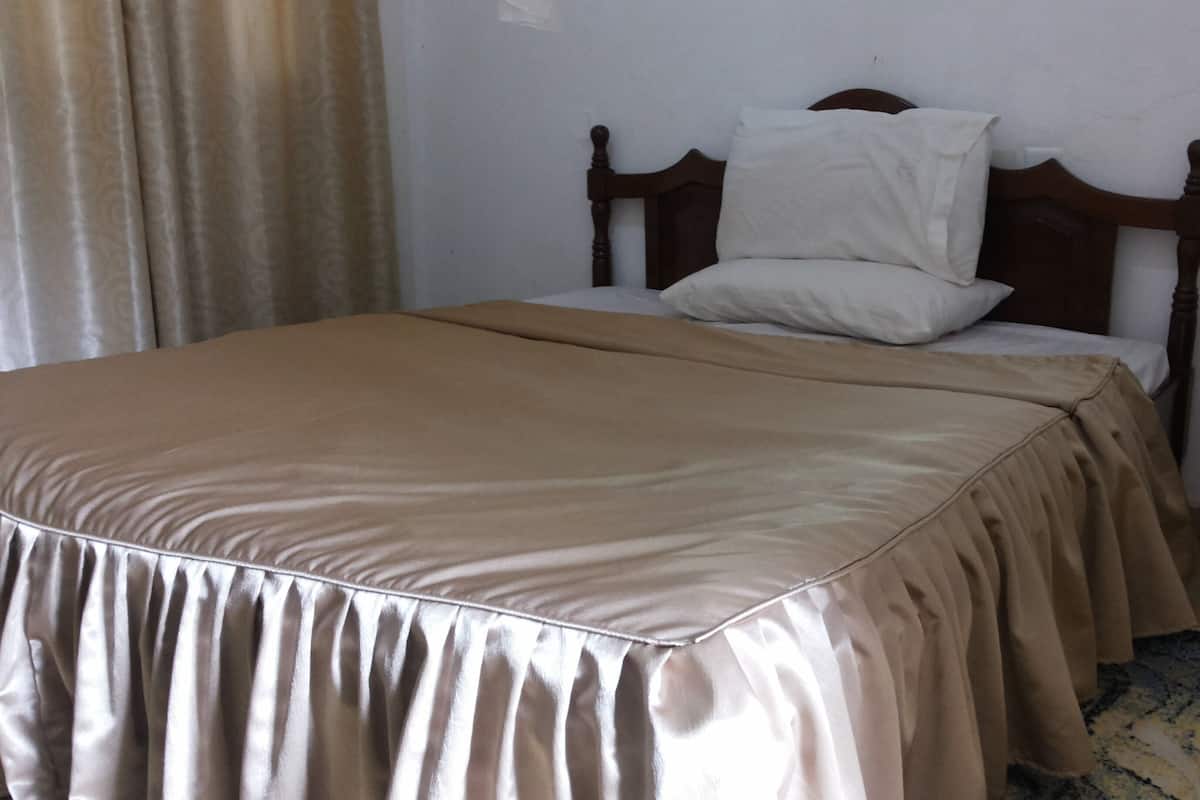 Una cama con cabecera de madera, colcha color beige y almohada blanca.
