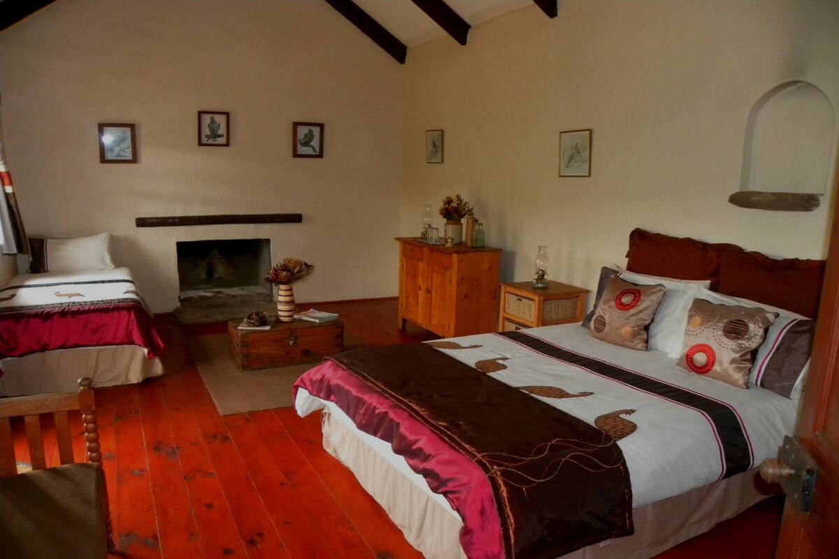 A room with two beds, a fireplace, wooden furniture, and wall-mounted artwork.