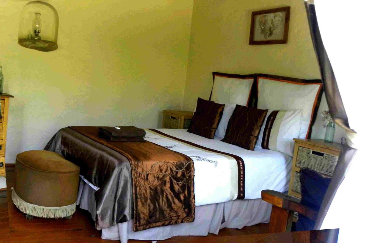 A bedroom with a bed, bedside tables, a nightstand, a lamp, and a wall-mounted shelf.