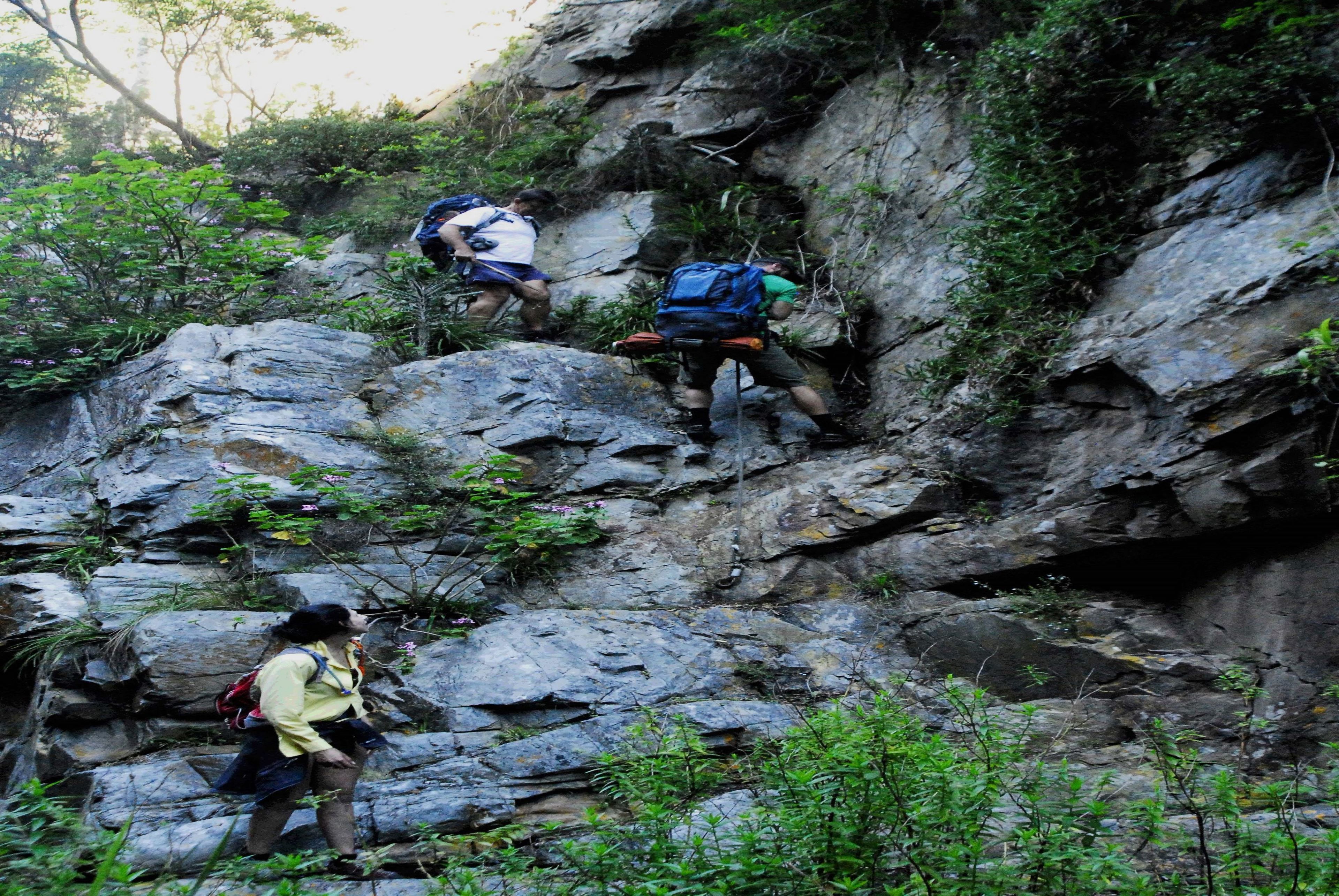 Three hikers ascending a rocky mountain path.
