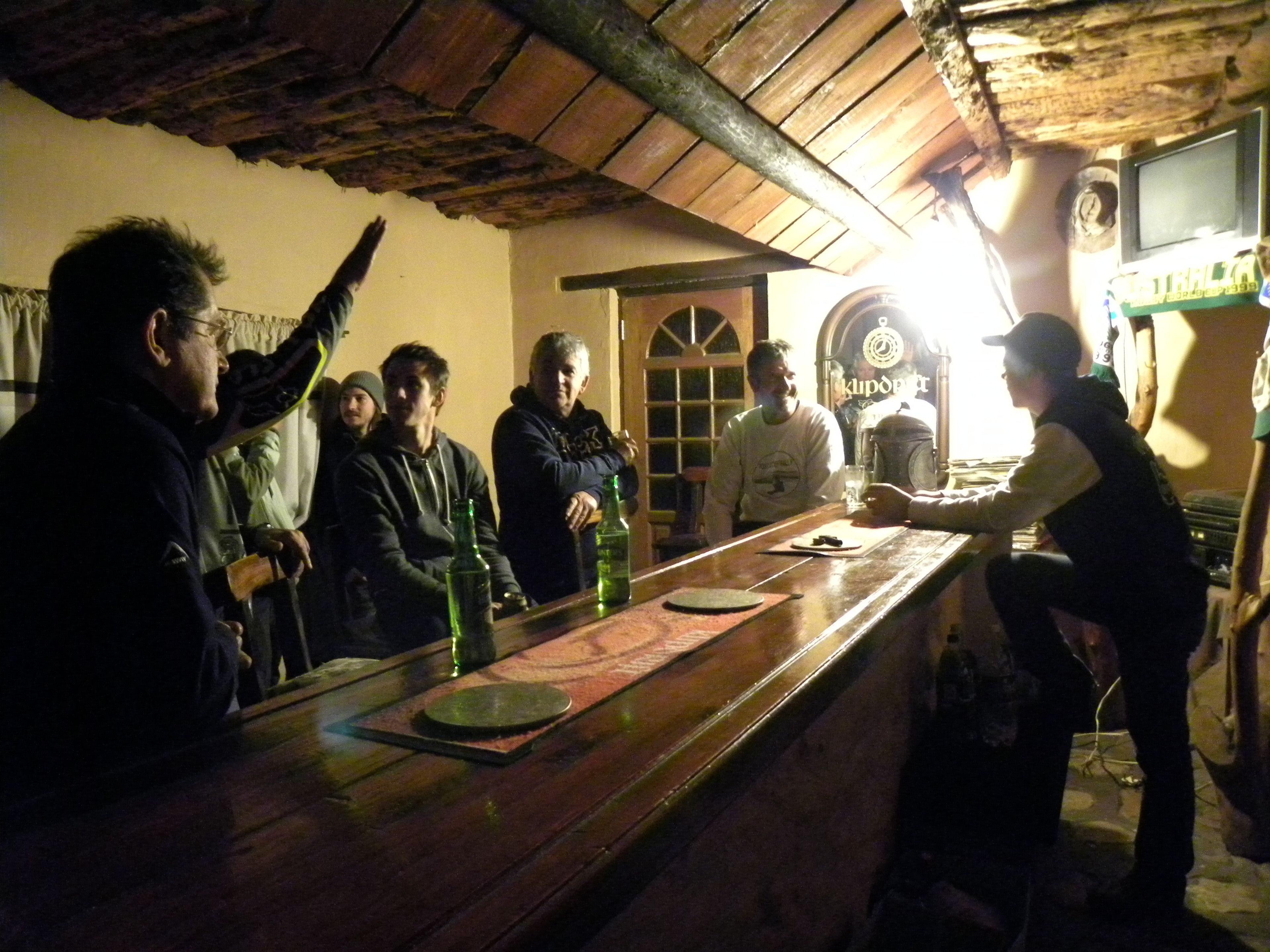 Un bar con mostrador de madera y decoración rústica, que incluye techo de madera y un reloj en la pared.