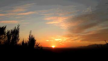Un coucher de soleil sur un paysage montagneux, avec les silhouettes d’arbres.