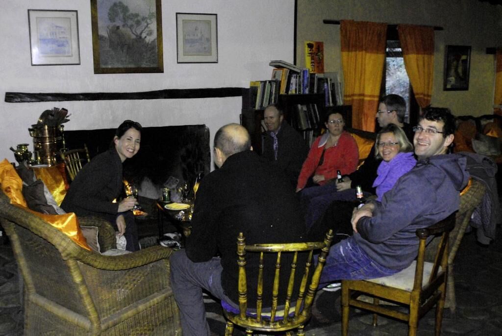 A group of people seated around a table in a room with wicker furniture and a bookshelf in the background.