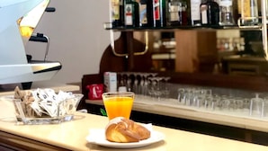 A bar area with a variety of liquor bottles on shelves, a coffee machine, and a breakfast setting with a croissant and orange juice. - Hotel Europa (Nocera Umbra)