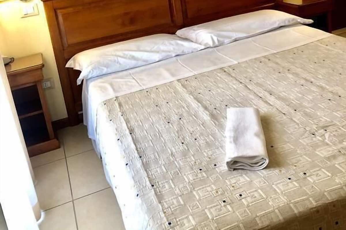 A neatly made bed with a patterned bedspread and a folded towel, a wooden headboard, two bedside lamps, and a framed picture on the wall.
