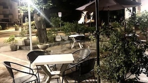 An outdoor seating area with tables and chairs under umbrellas, surrounded by potted plants and a tree. - Hotel Europa (Nocera Umbra)