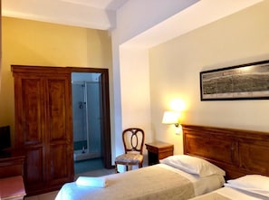 A hotel room with a bed, a chair, a wooden wardrobe, a shower, and a wall-mounted lamp. - Hotel Europa (Nocera Umbra)