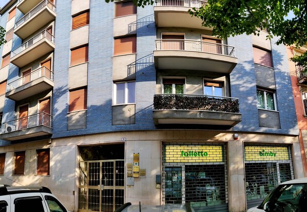 A multi-story building with balconies, a ground-level shop with 'folletto' and 'bimby' signs, and a gated entrance. - B&B Valverde (Verona)