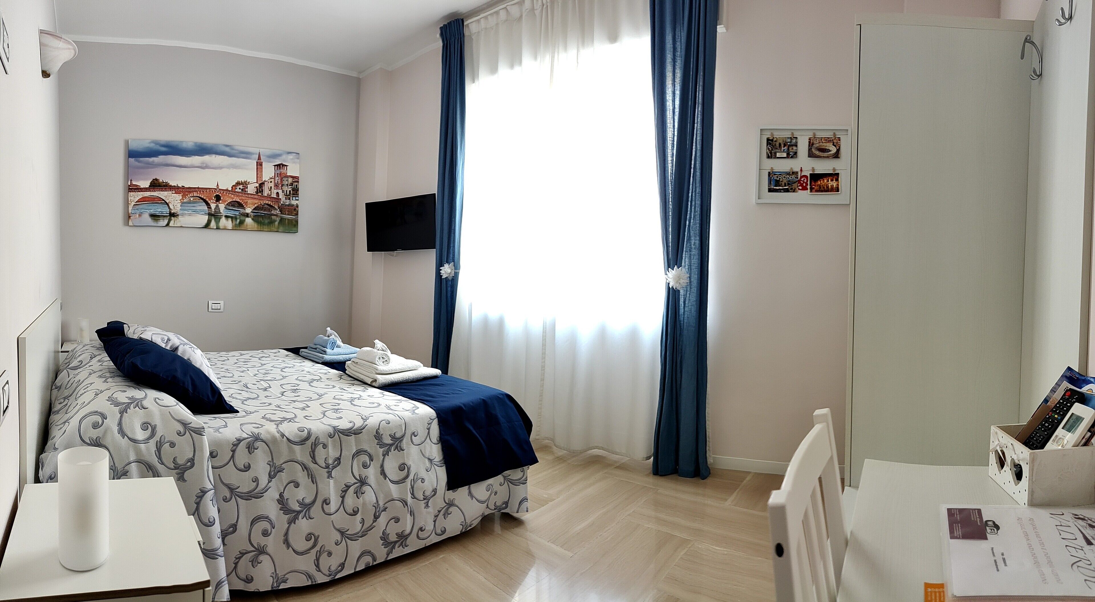 A bedroom with a bed, a bedside table, a TV, a window with curtains, and a wall with pictures.