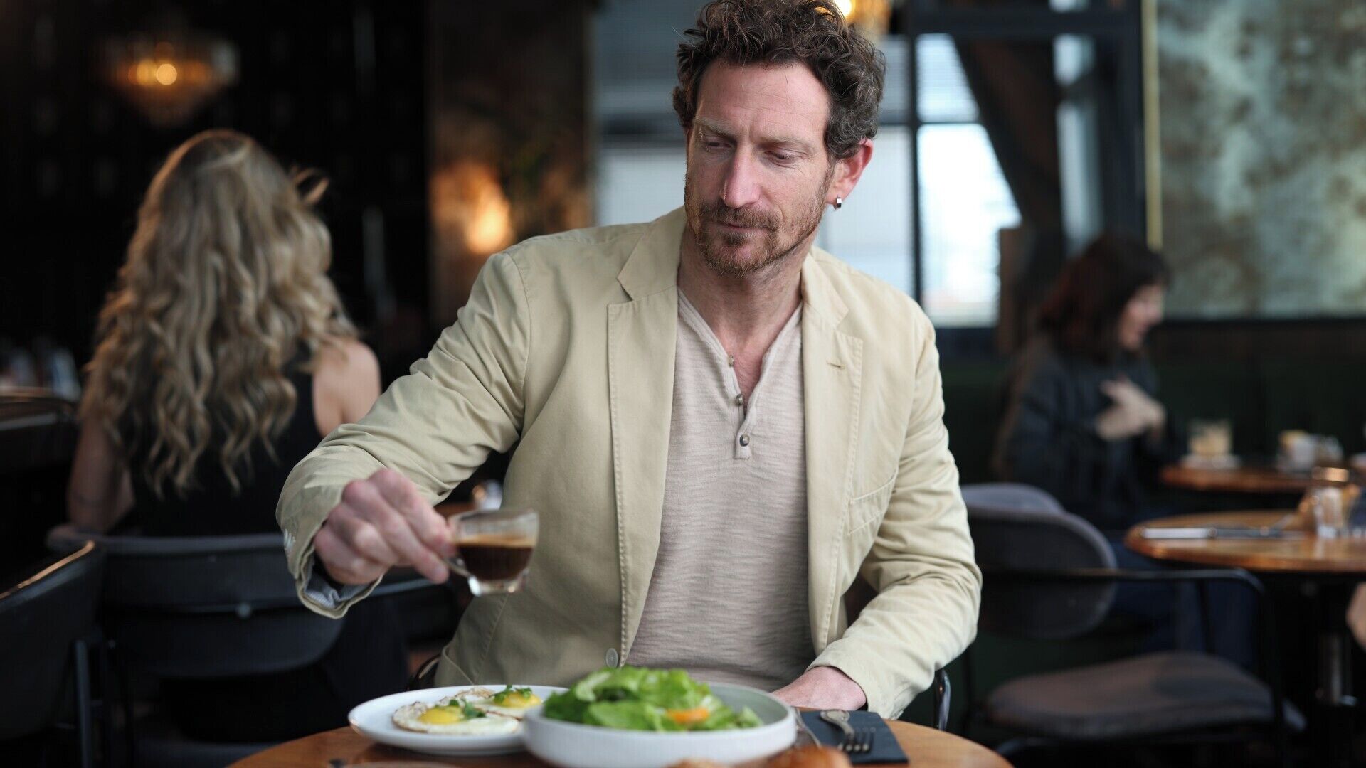 A person dining in a restaurant with a table, chairs, and other diners in the background.