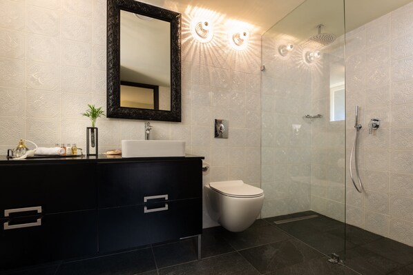 A modern bathroom with a black vanity, a white toilet, and a glass-enclosed shower area. - Bachar House - FATTAL COLORS (Tel Aviv)
