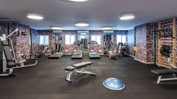 A gym with various exercise equipment, brick-patterned walls, and large windows.