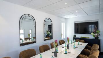 A conference room with a long table, brown chairs, a large flat-screen TV, and two wall-mounted mirrors.