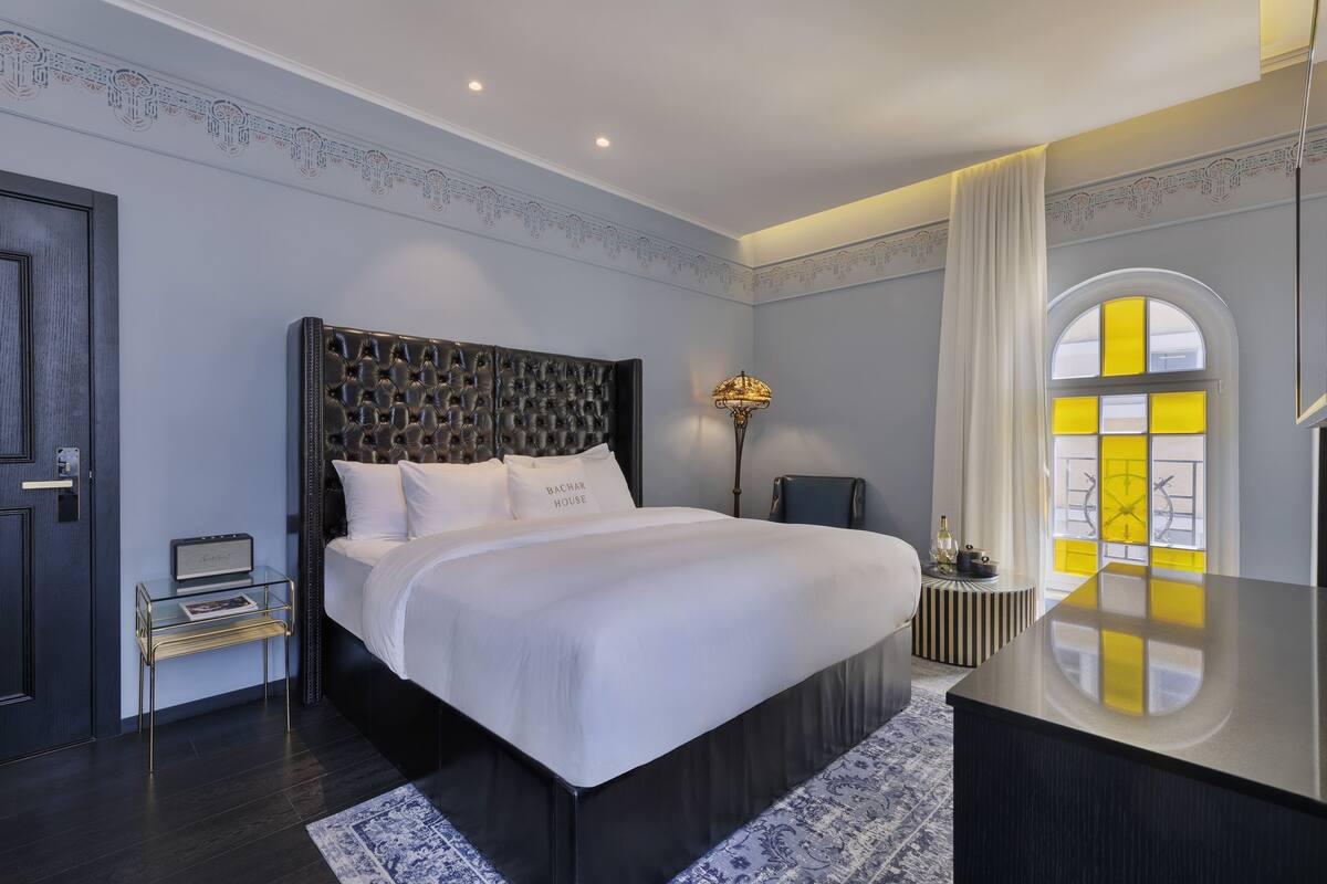 A modern bedroom with a large bed, a bedside table, a lamp, and a view of the outside through a window.