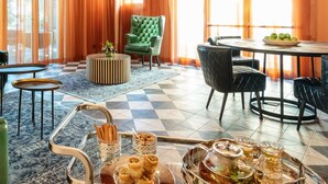 A modern lounge area with leather sofas, a round table with a fruit bowl, and a tray of pastries. - Bachar House - FATTAL COLORS (Tel Aviv)