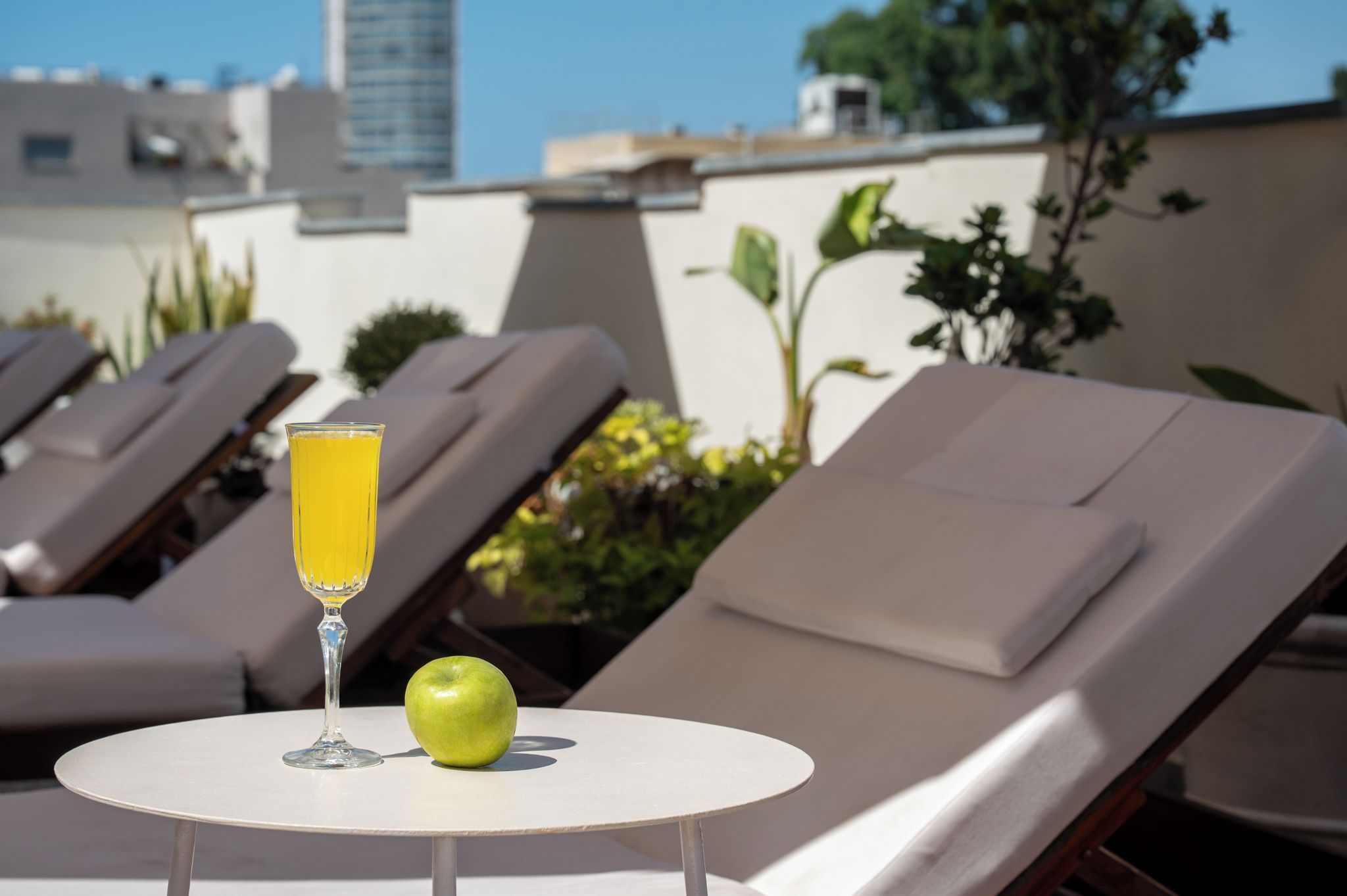 Een zonnig buitenzitgedeelte met lounge fauteuils, een tafel met een glas jus d'orange en een groene appel.
