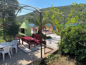 A patio with a grill, tables, and chairs, overlooking a body of water and hills.
